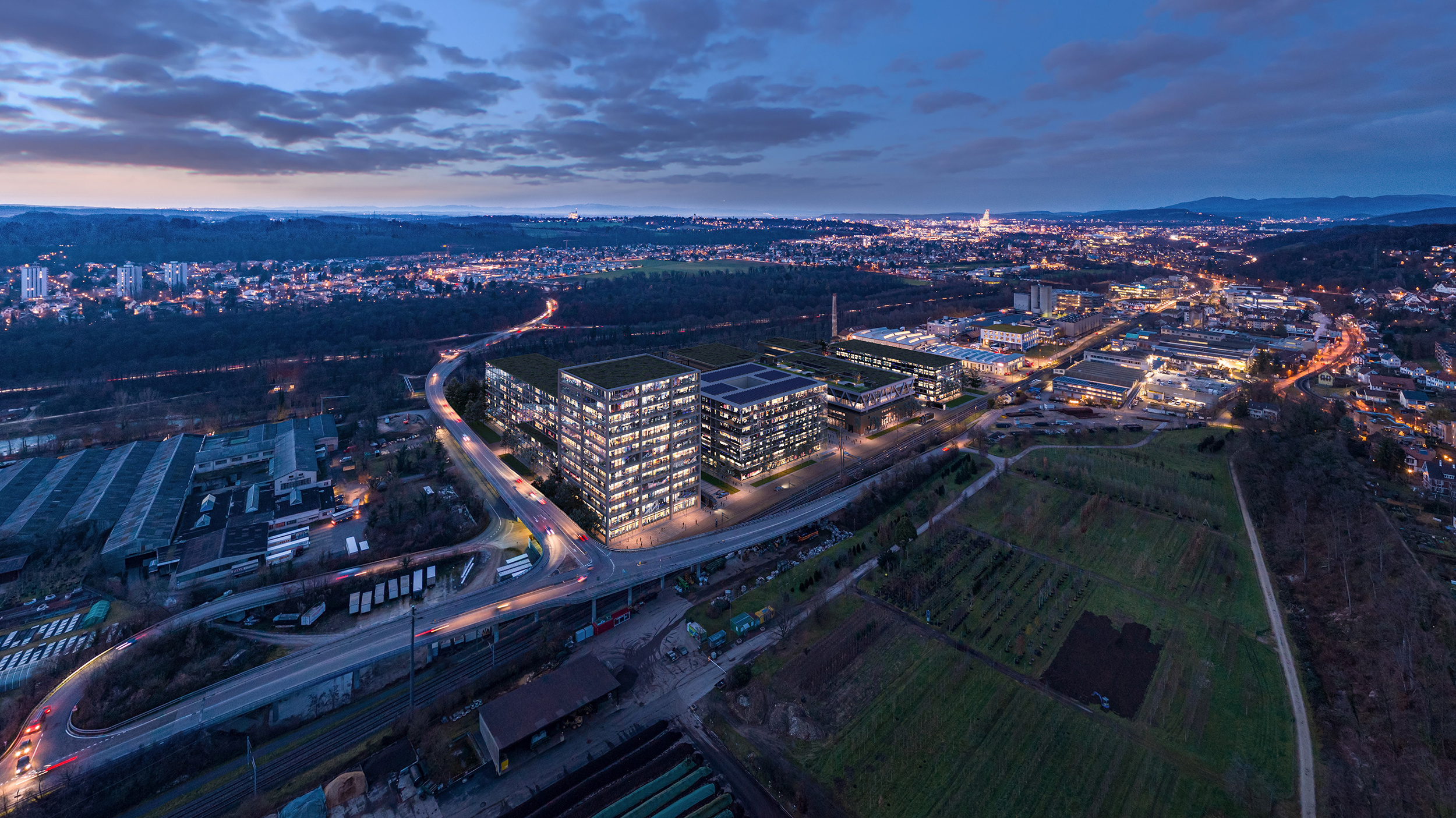 Aerial view of the uptownBasel innovation campus at dusk in Arlesheim near Basel – the illuminated campus on the A18 with views over the Basel region