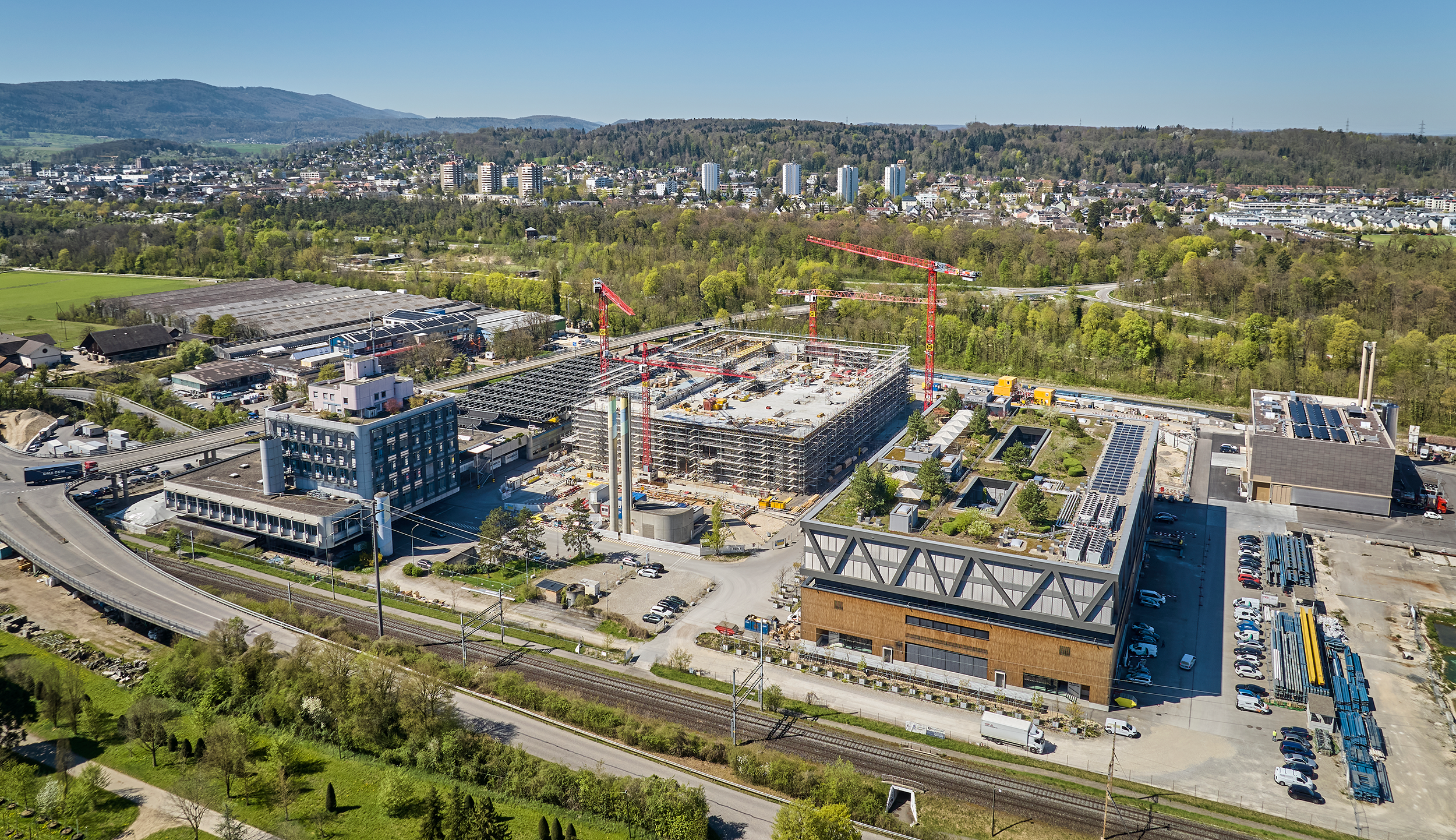 Luftaufnahme des uptownBasel Areals in Arlesheim im Frühling 2026 – Gebäude 1 fertiggestellt, Gebäude 2 im Bau, mit Bahnlinie und Autobahnanschluss